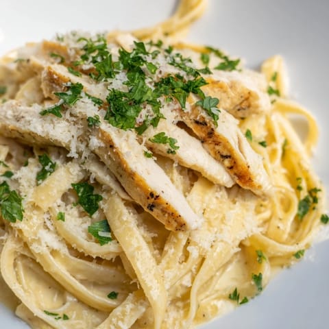 Tender chicken sits atop a bed of creamy fettuccine Alfredo, garnished with fresh parsley and cheese.