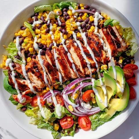 A close-up of BBQ Chicken Salad shows creamy avocado slices and shredded cheese atop the greens, with ranch drizzle glinting in the light.