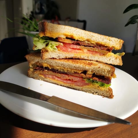 A close-up of a sliced Vegan Bacon BLT Grilled Cheese, revealing melted vegan cheese and layers of fresh vegetables served warm on a plate.