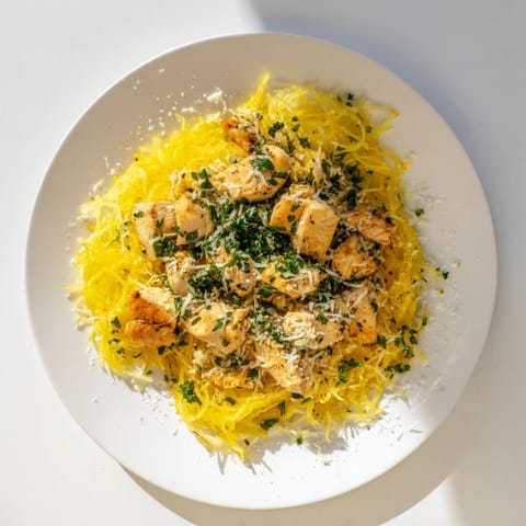 A close-up of lemon garlic chicken sizzling in a skillet, releasing fragrant steam beside forked spaghetti squash noodles.