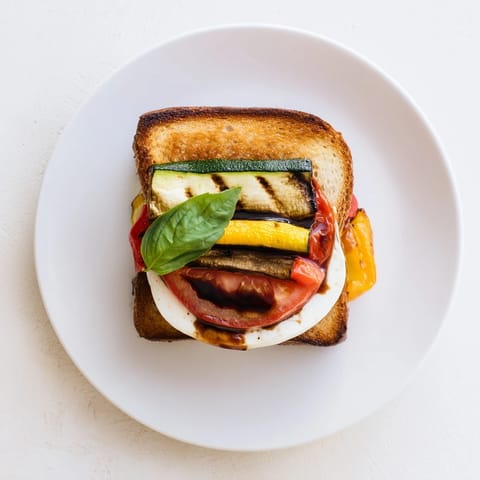 Golden-brown sourdough slices stuffed with melted mozzarella, roasted zucchini, peppers, and fresh basil for a Roasted Veggie Caprese Grilled Cheese.
