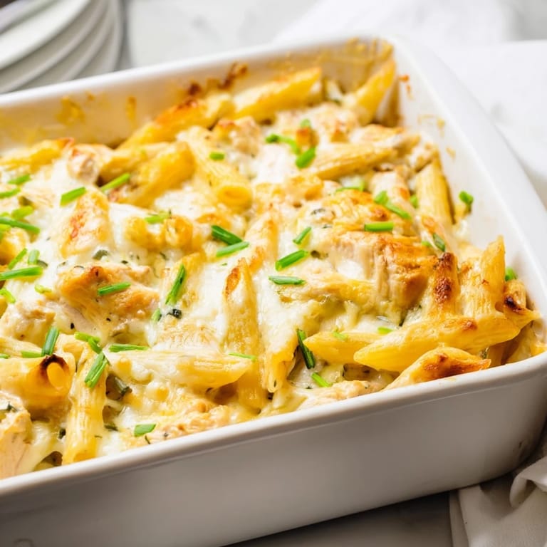 Spoon lifting a cheesy bite of Chicken Ranch Pasta Bake, revealing layers of pasta and chicken.