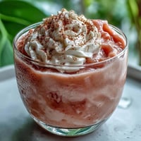 Creamy Guava Coquito in a glass bottle, garnished with ground cinnamon and a cinnamon stick for a festive Puerto Rican holiday drink.
